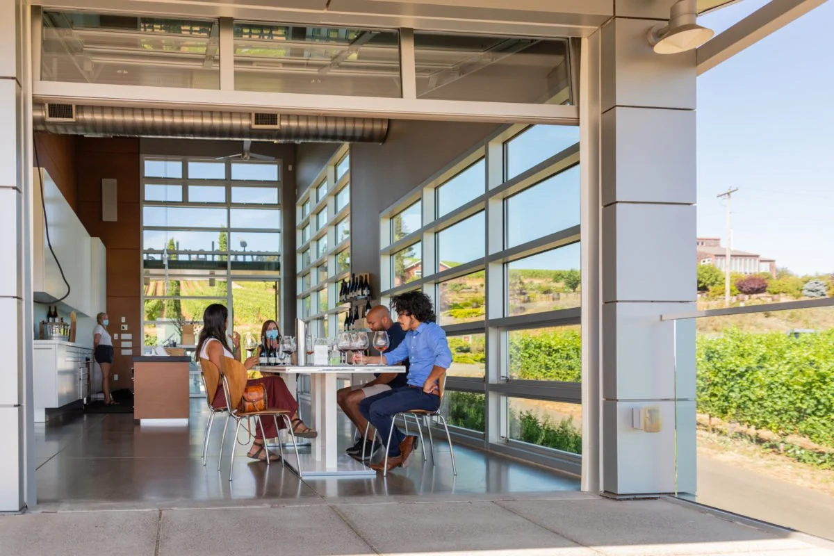 People dining at a restaurant with large windows showing a green landscape outside.