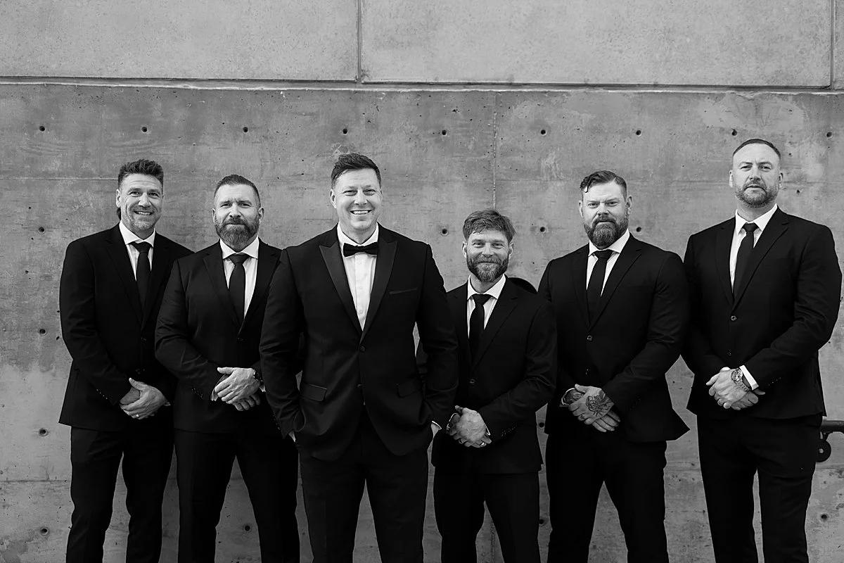 Groom laughing with his groomsmen dressed in black suits at Monte Creek Winery in Kamloops, BC