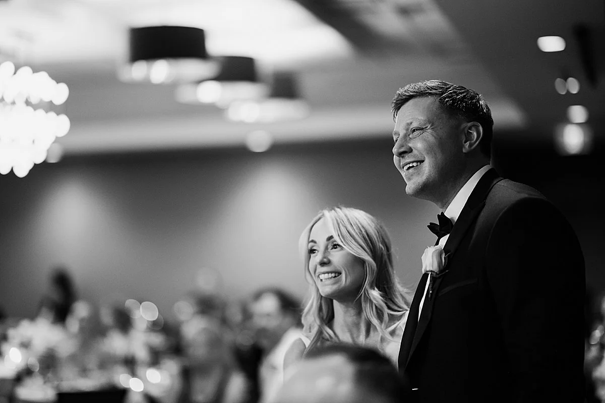 bride and groom photographed listening to speeches at wedding reception