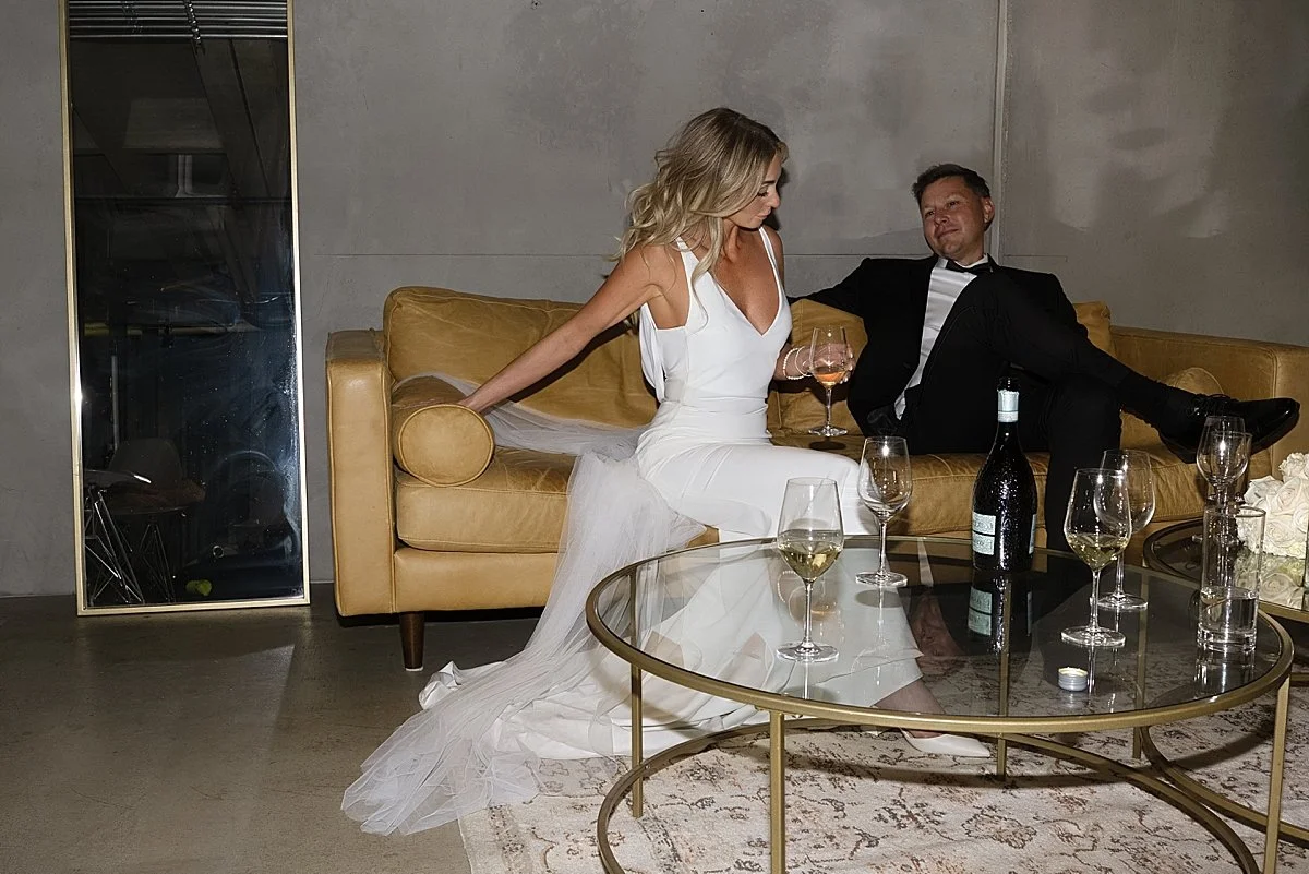 Bride and groom relaxing on a couch with wine glasses during their stylish Kamloops wedding reception at the Delta Hotel