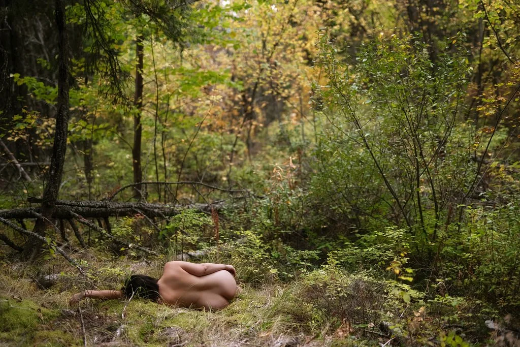 woman laying on grass in a forest naked with her back to the camera