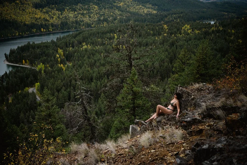 woman sitting up against some rocks with a beautiful view of the lake and trees behind her