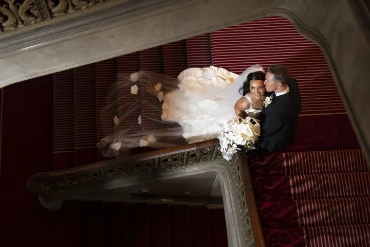 Bride and groom embracing on an ornate staircase of Hotel Cleveland, viewed from above