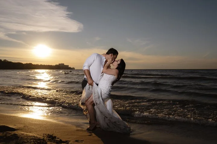 Newlywed couple kissing in wedding attire on a beach at sunset