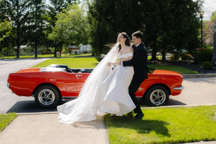 Bride and groom posing beside a red vintage convertible on a sunny street