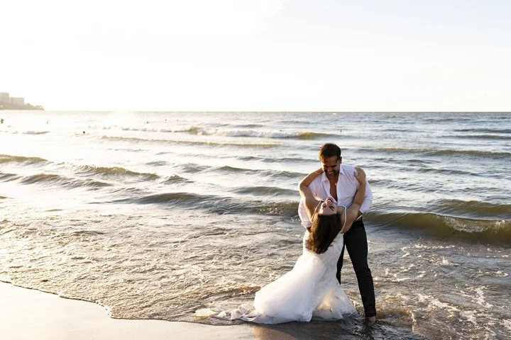 Newlywed couple embracing in shallow ocean waves on a beach at sunset for a trash the dress session