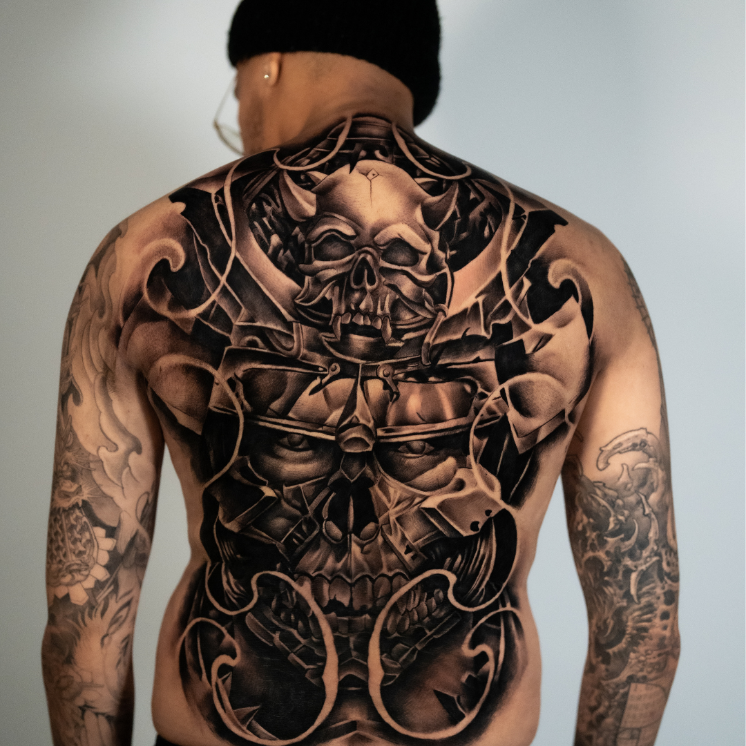A person with a large, intricate black and gray tattoo covering their back and arms, featuring a Japanese back tattoo