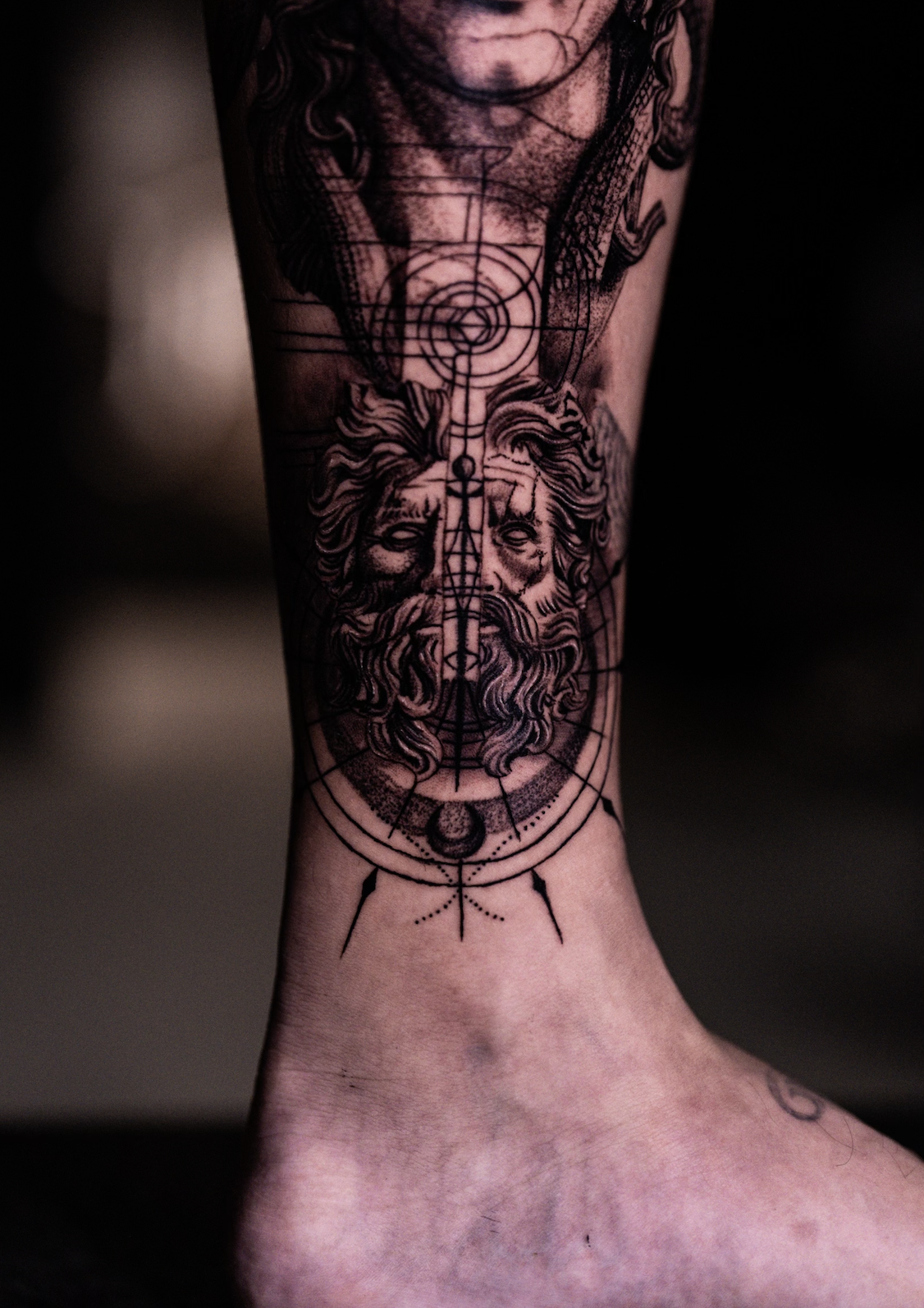Detailed tattoo on leg with a geometric design and a face illustration, featuring intricate line work and shading.