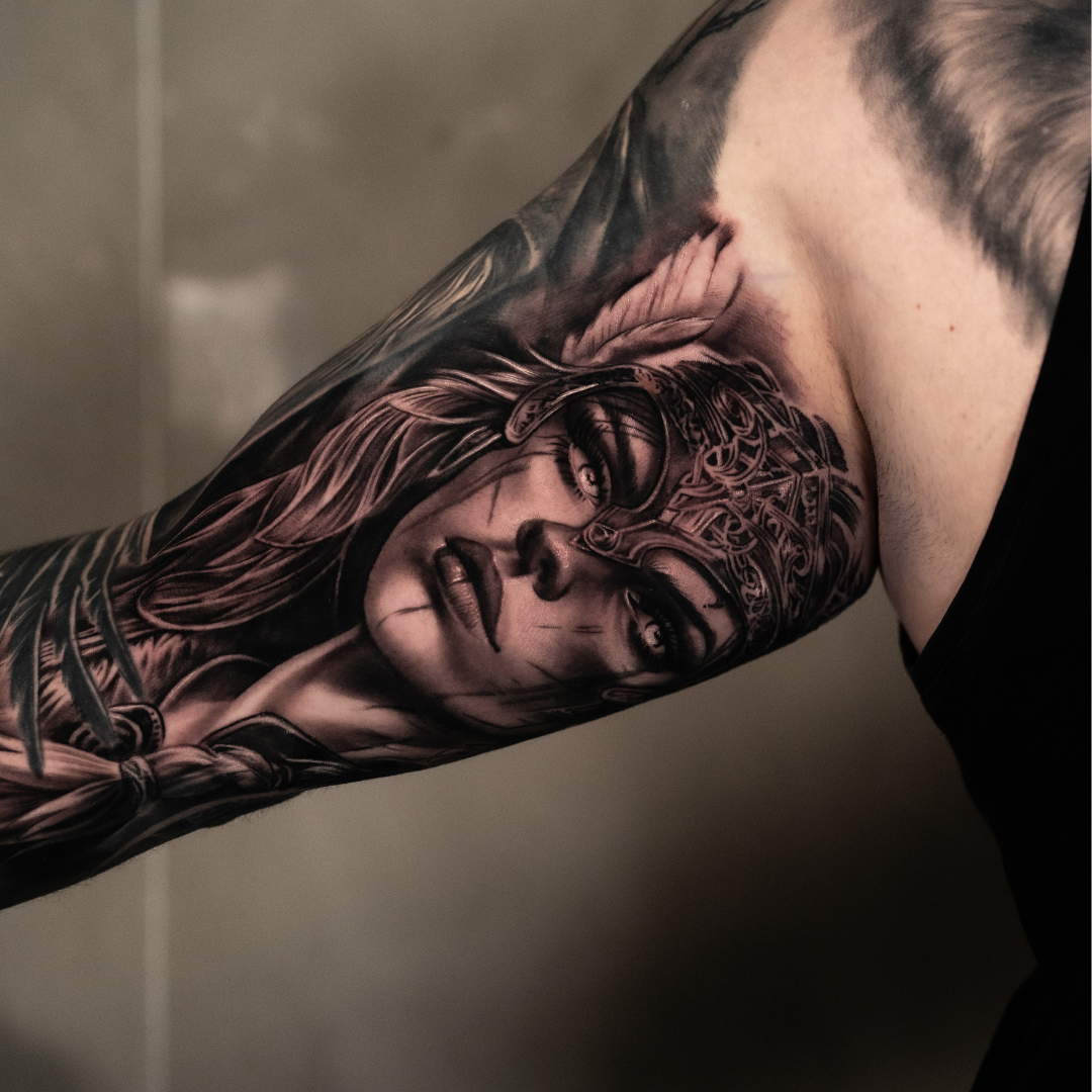 Black and grey tattoo of a woman with long hair, wearing a headpiece, on a person's arm.