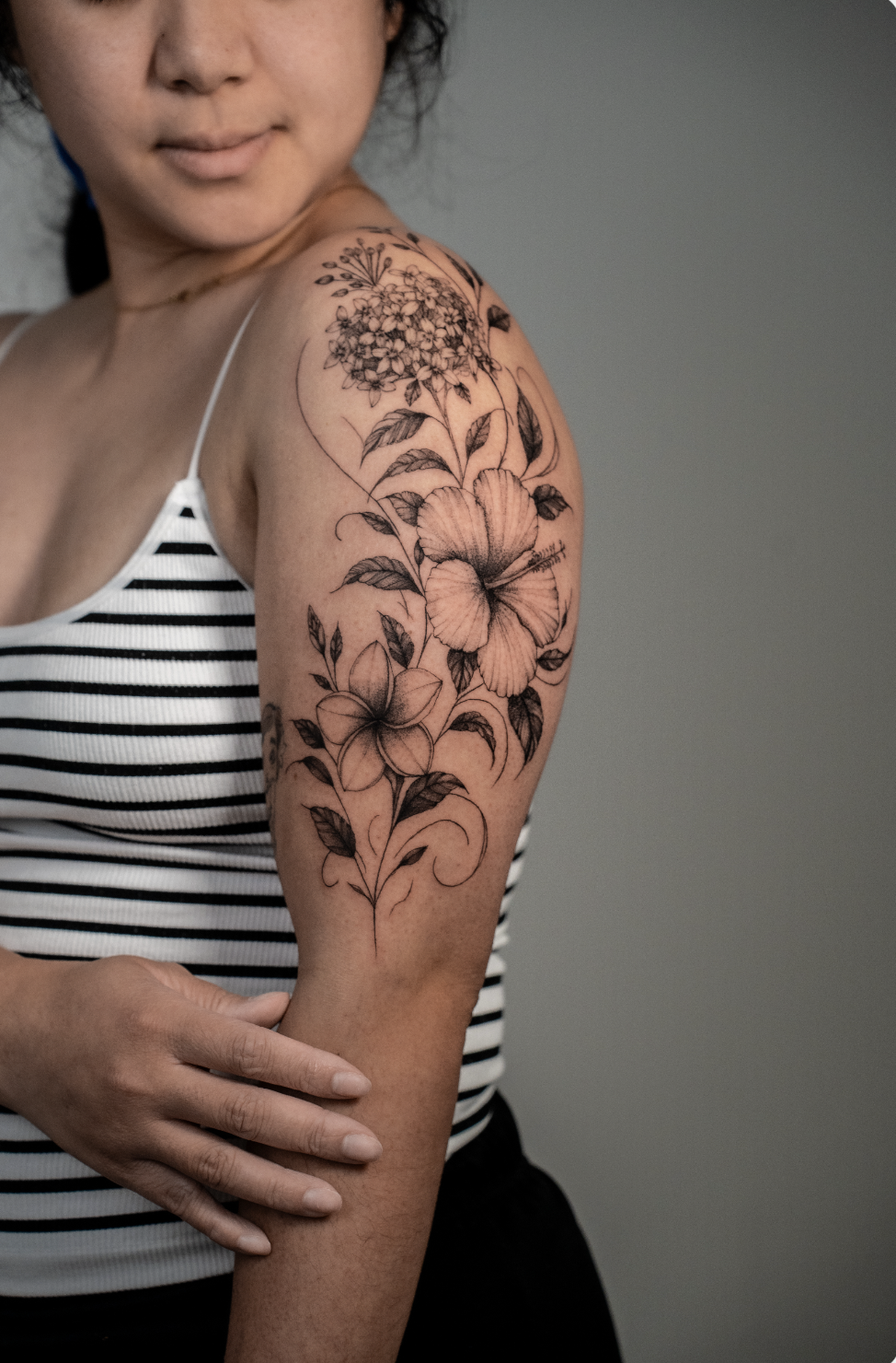 A woman with a floral tattoo on her upper arm, wearing a black and white striped tank top.