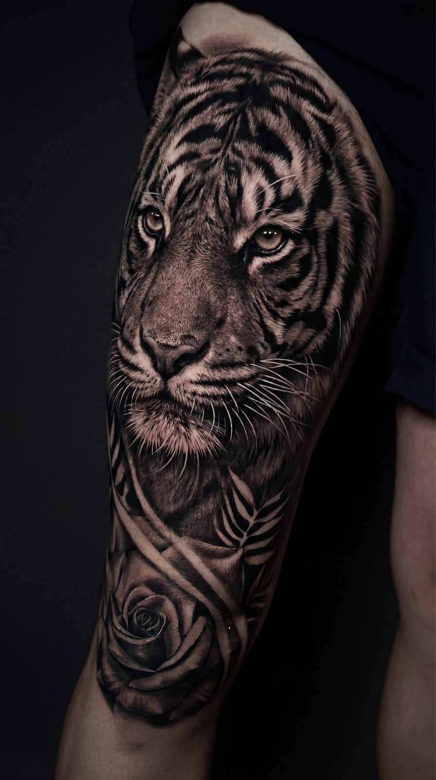 Leg tattoo ideas for guys featuring a black and grey realism tiger thigh tattoo with detailed fur shading intense eyes and a rose element for a bold masculine leg sleeve design