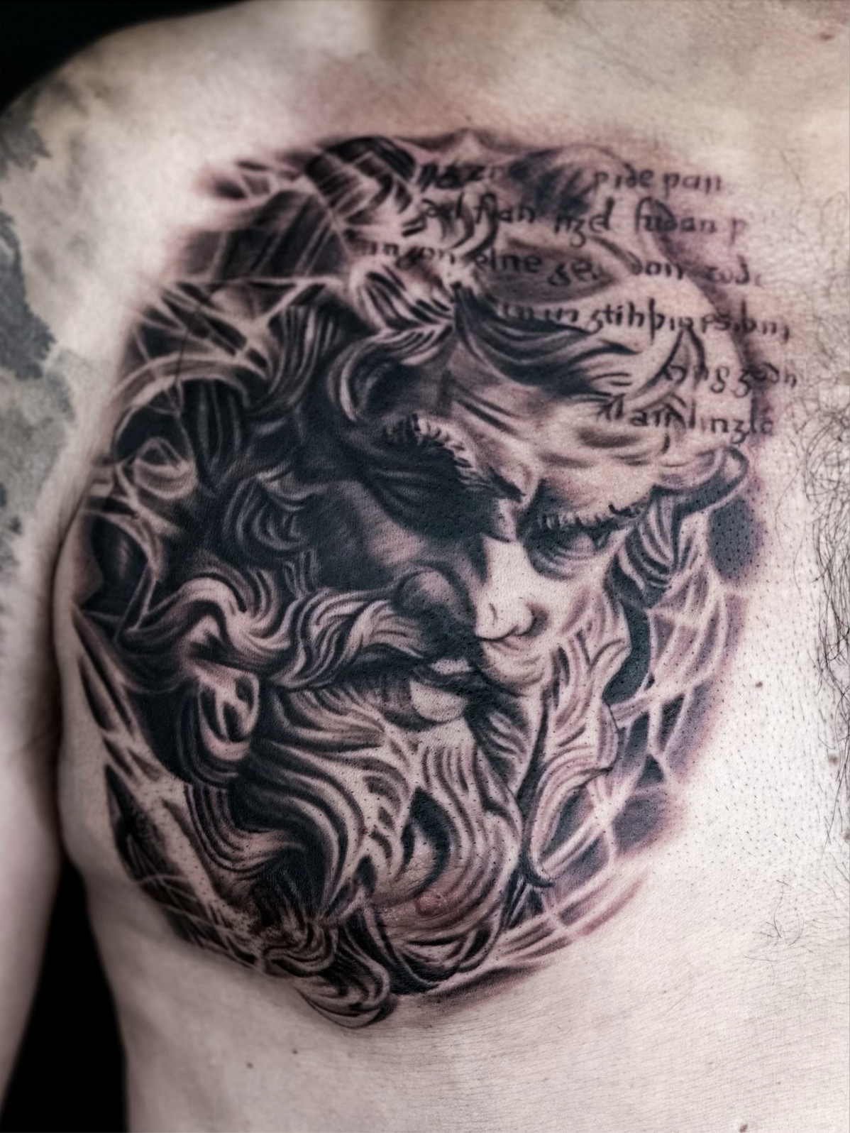 chest tattoo of Zeus with detailed hair and beard in black and gray ink