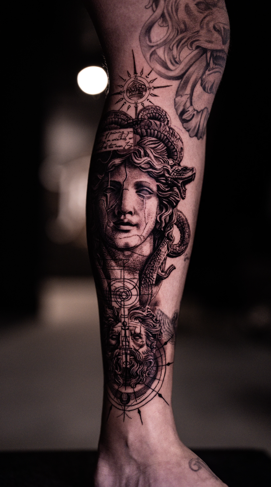 Tattoo of mythological faces on a calf, dark background