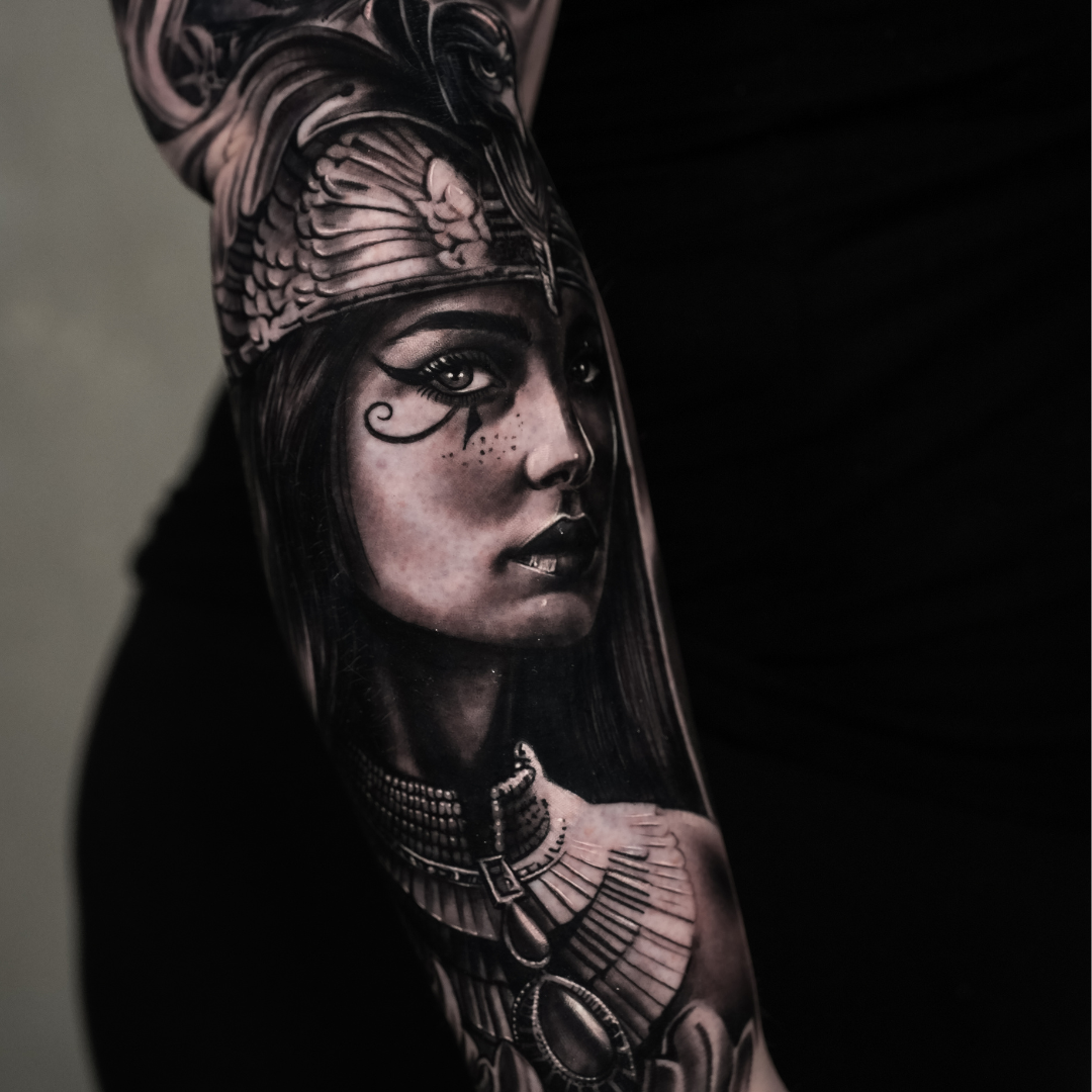 Black and gray realistic tattoo of a woman wearing an Egyptian headdress with jewelry, on a person's arm.
