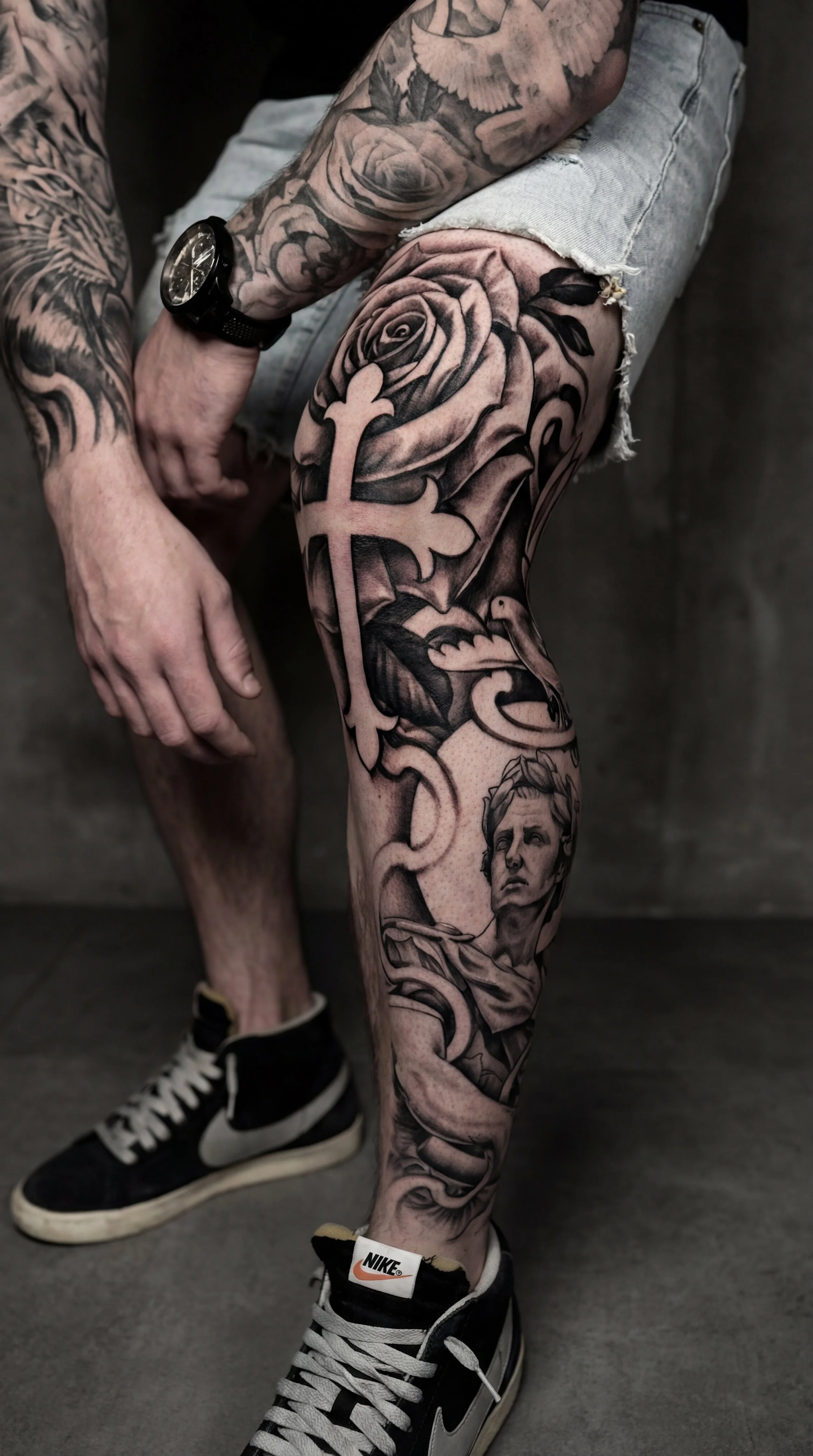 Leg tattoo ideas for guys featuring a black and grey rose knee tattoo with bold petals smooth shading and circular flow designed to fit the kneecap and connect into a leg sleeve