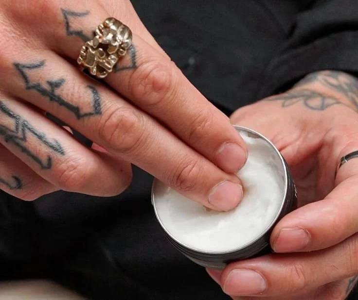 Tattoo aftercare ointment being applied to a fresh black and grey realism tattoo during healing