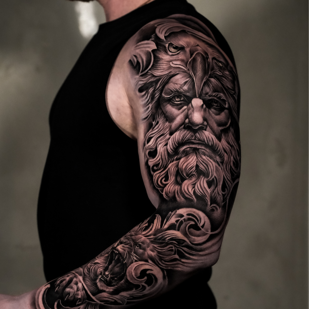 Black and gray tattoo of a bearded man with a lion and an eagle on his head, and a roaring lion on his forearm.