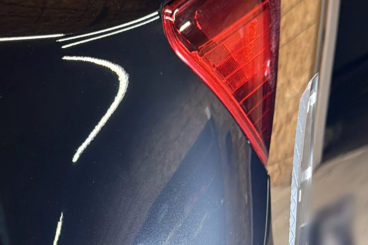 After paint correction: the black Subaru rear quarter panel is glossy and clear, with the shop lights reflecting sharply.