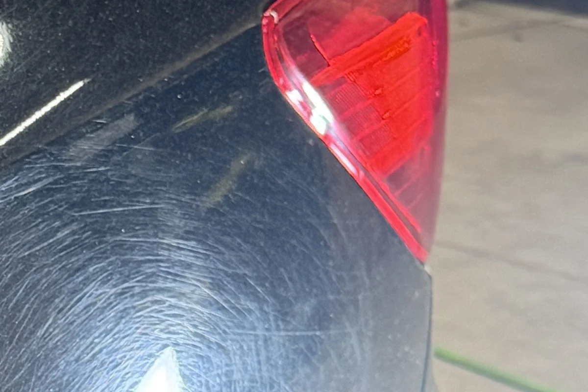 Before paint correction: the same black Subaru rear quarter panel covered in heavy circular swirl marks and fine scratches.