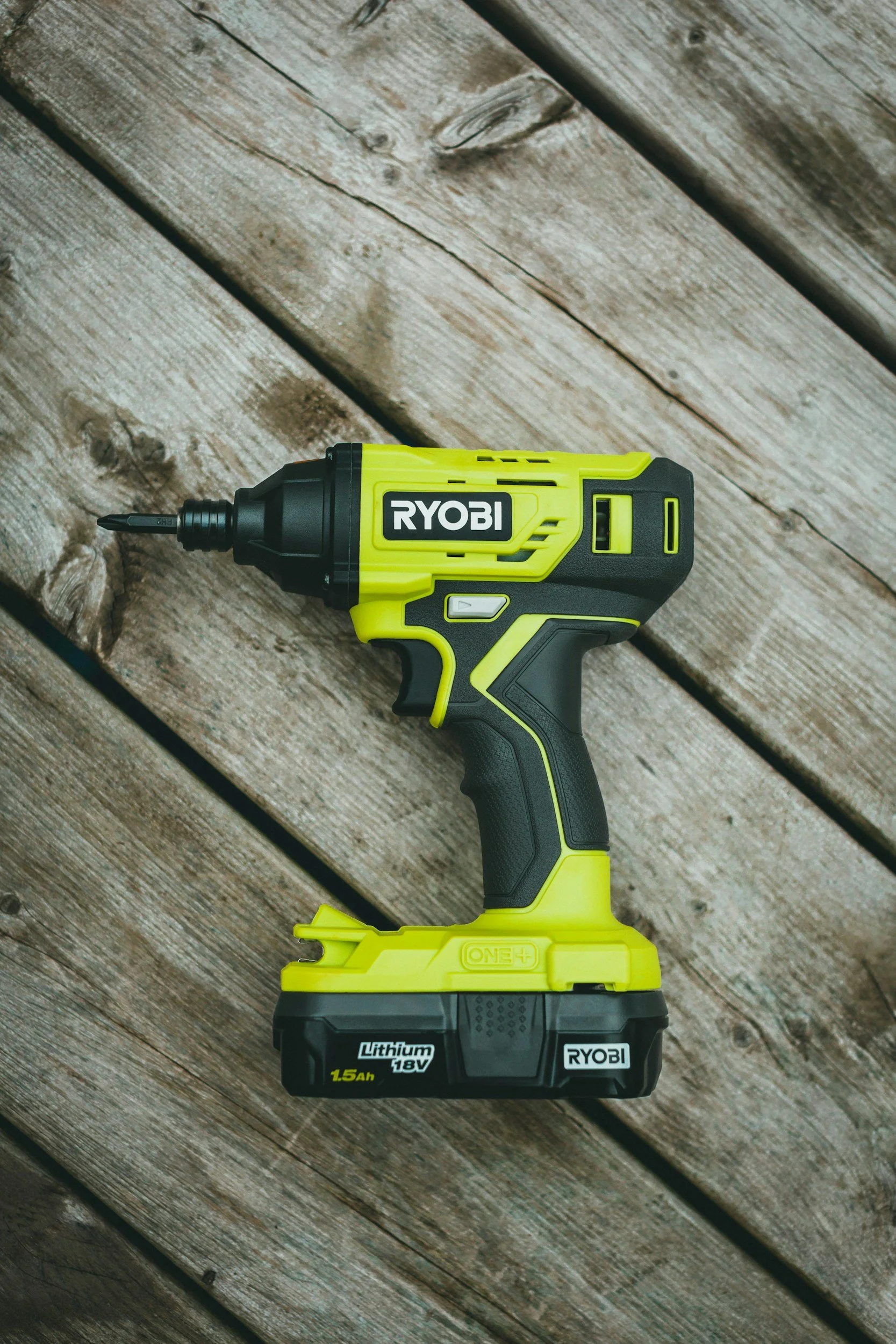 A yellow and black Ryobi cordless power drill resting on a weathered wooden surface.