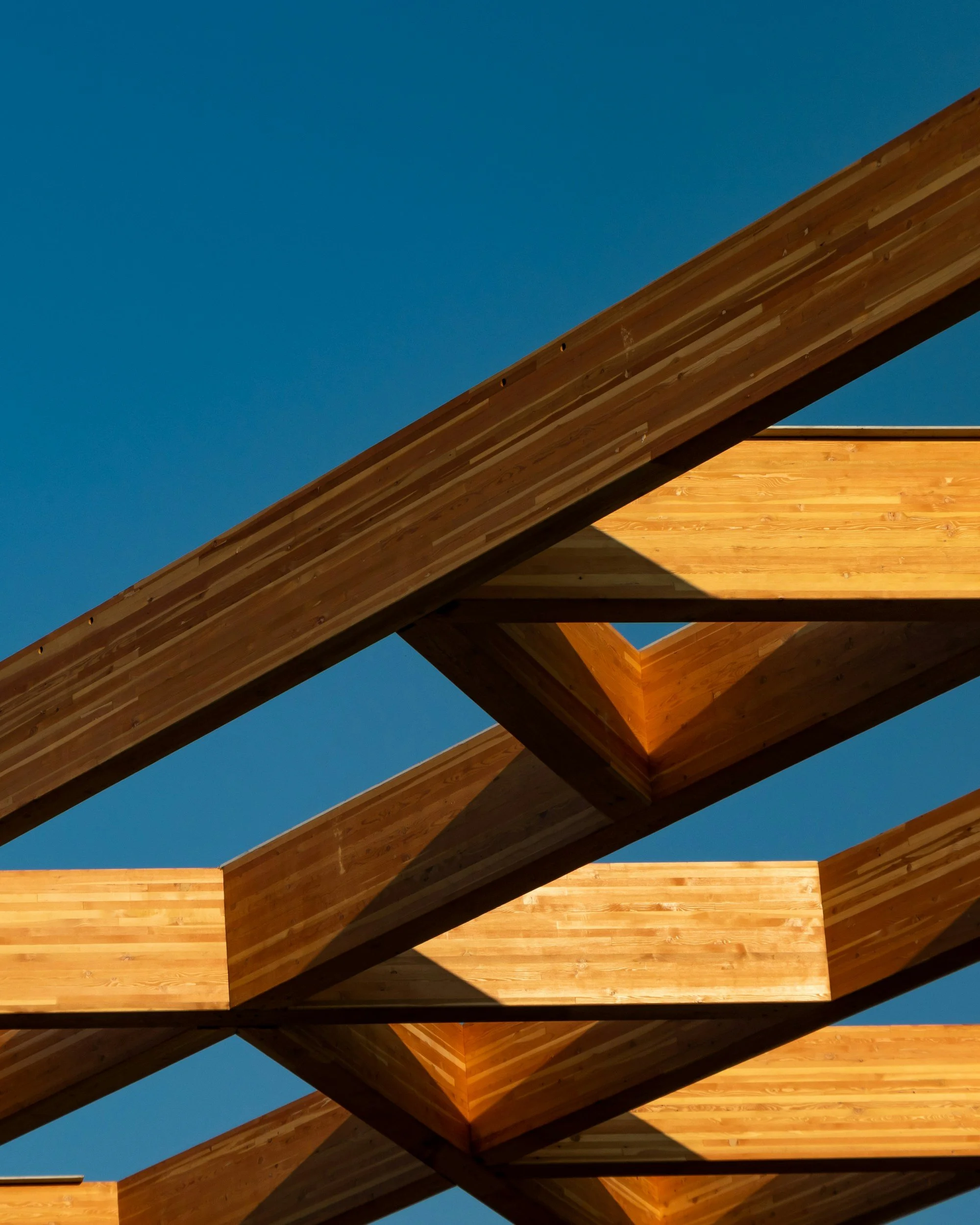 A modern architectural structure with a wooden roof, featuring sharp angles and geometric shapes, against a clear blue sky.