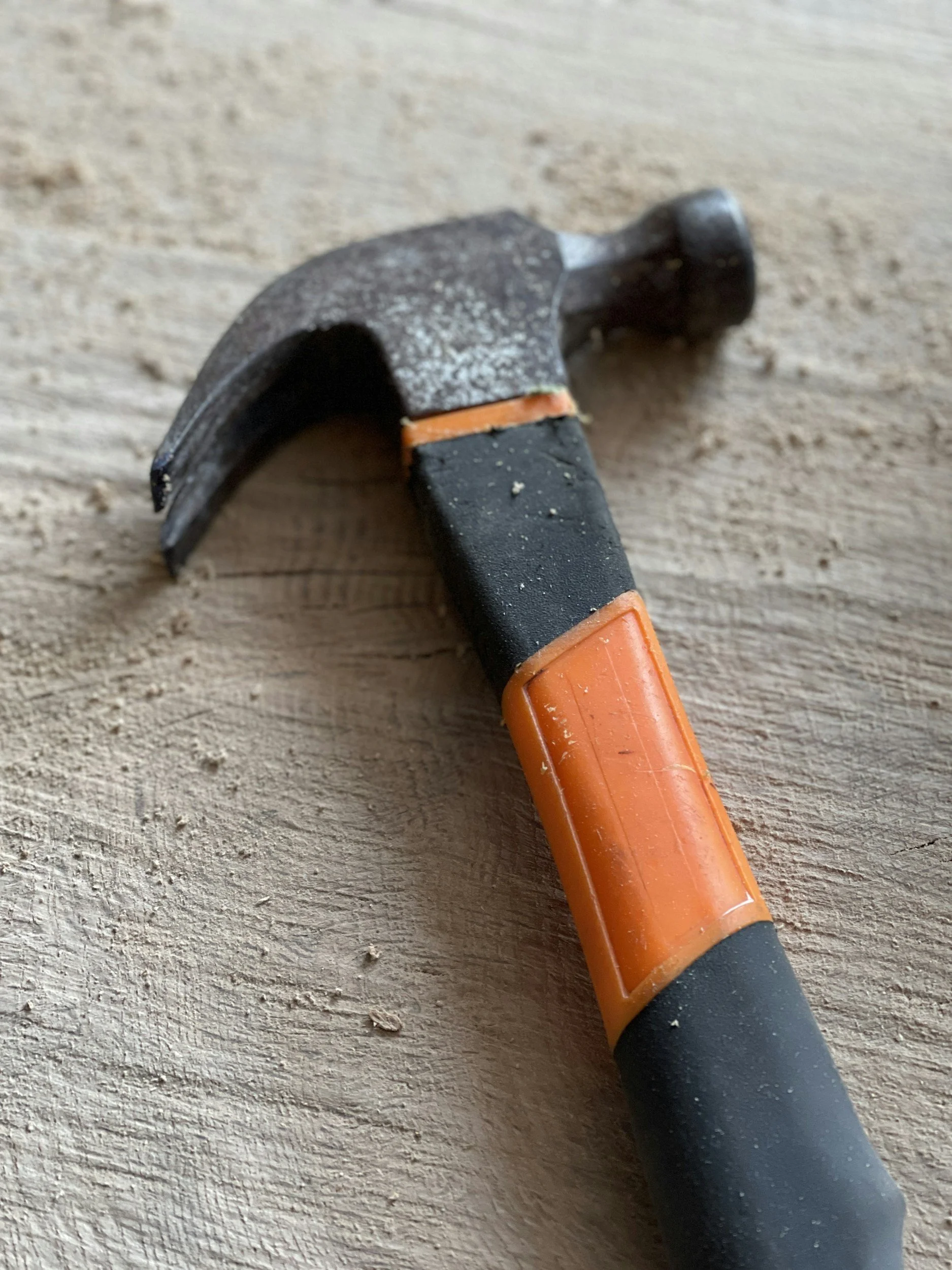 A hammer with a black handle, orange accents, and a metal head resting on a wooden surface.