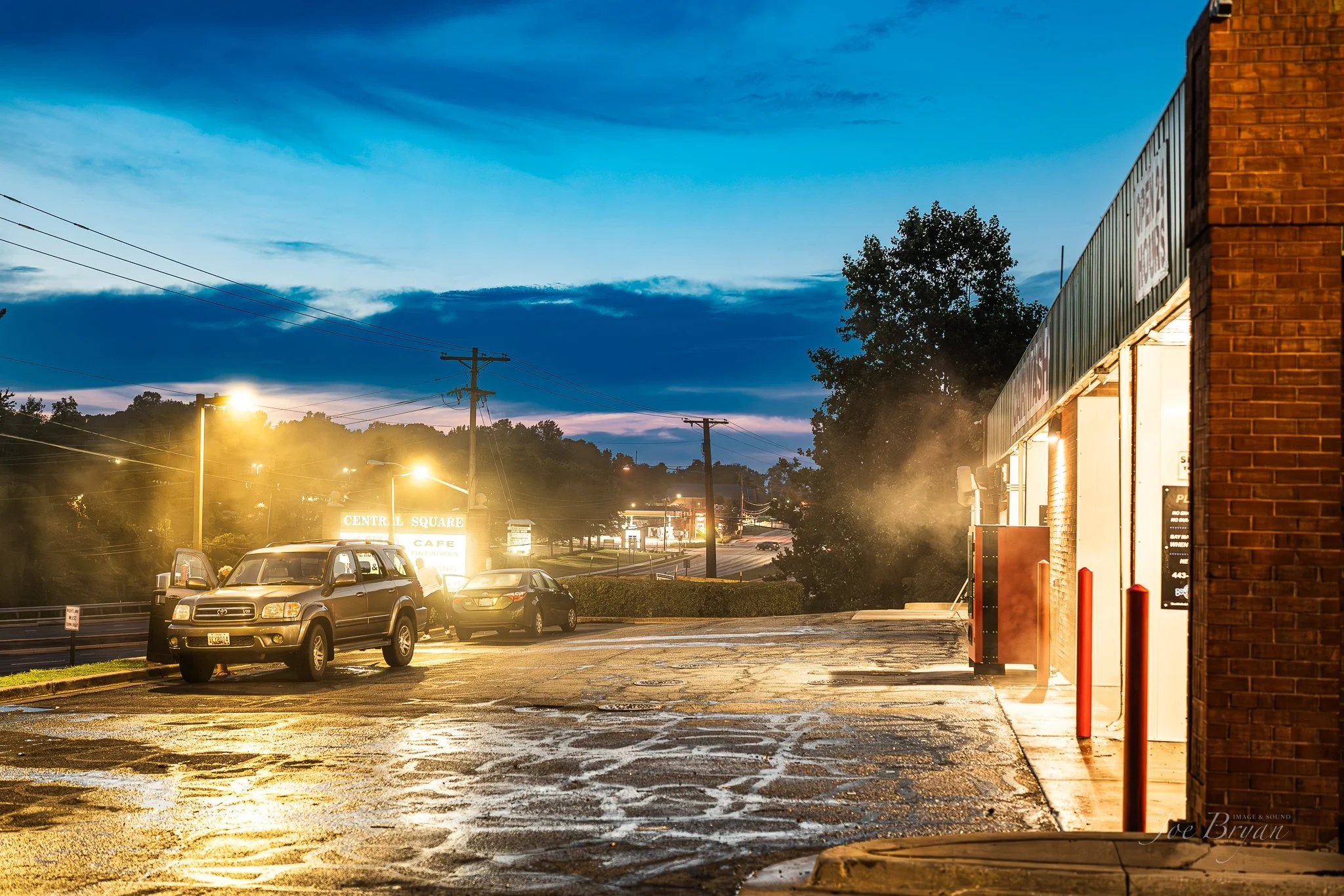 Nighttime parking lot with cars, streetlights, brick building, and "Centre Square Cafe" sign in the background.