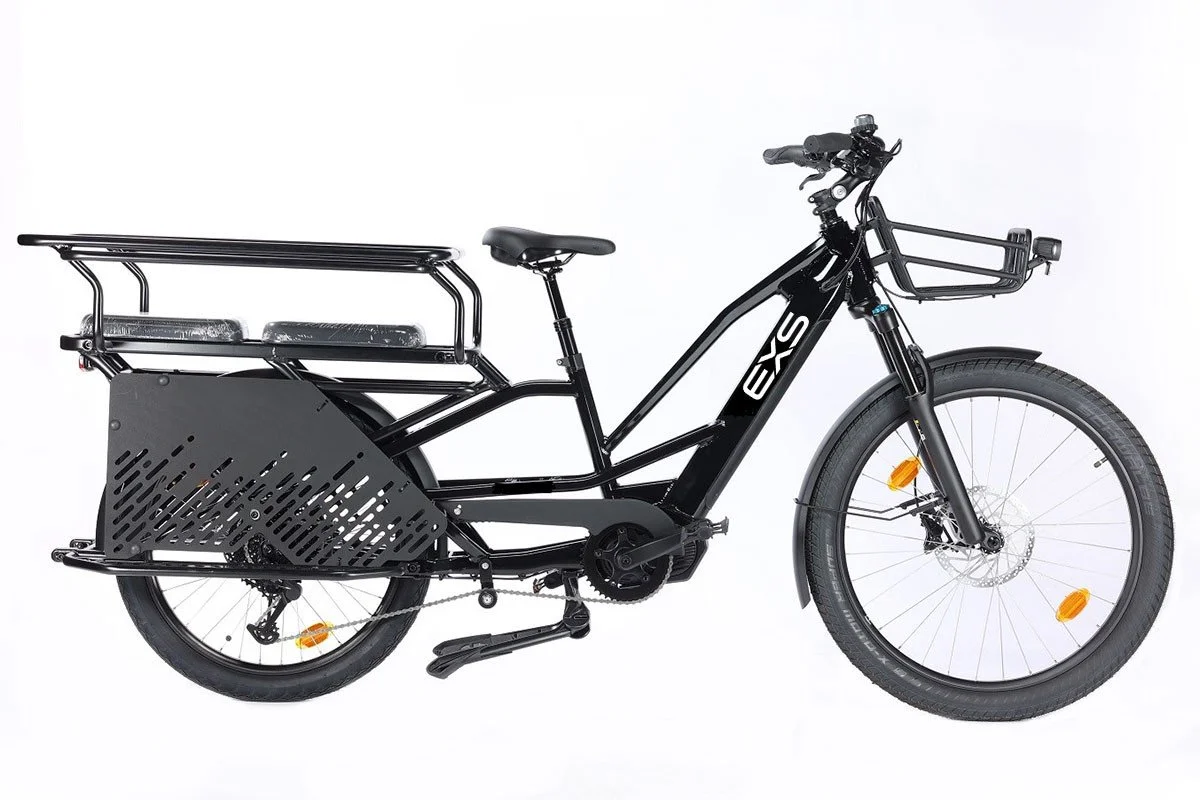 Vélo électrique noir avec un panier à l'avant, une plateforme garnie en dessous du siège pour le transport, et un chargement à l'arrière avec une grille. Structure robuste, pneus larges adaptés aux terrains urbains.