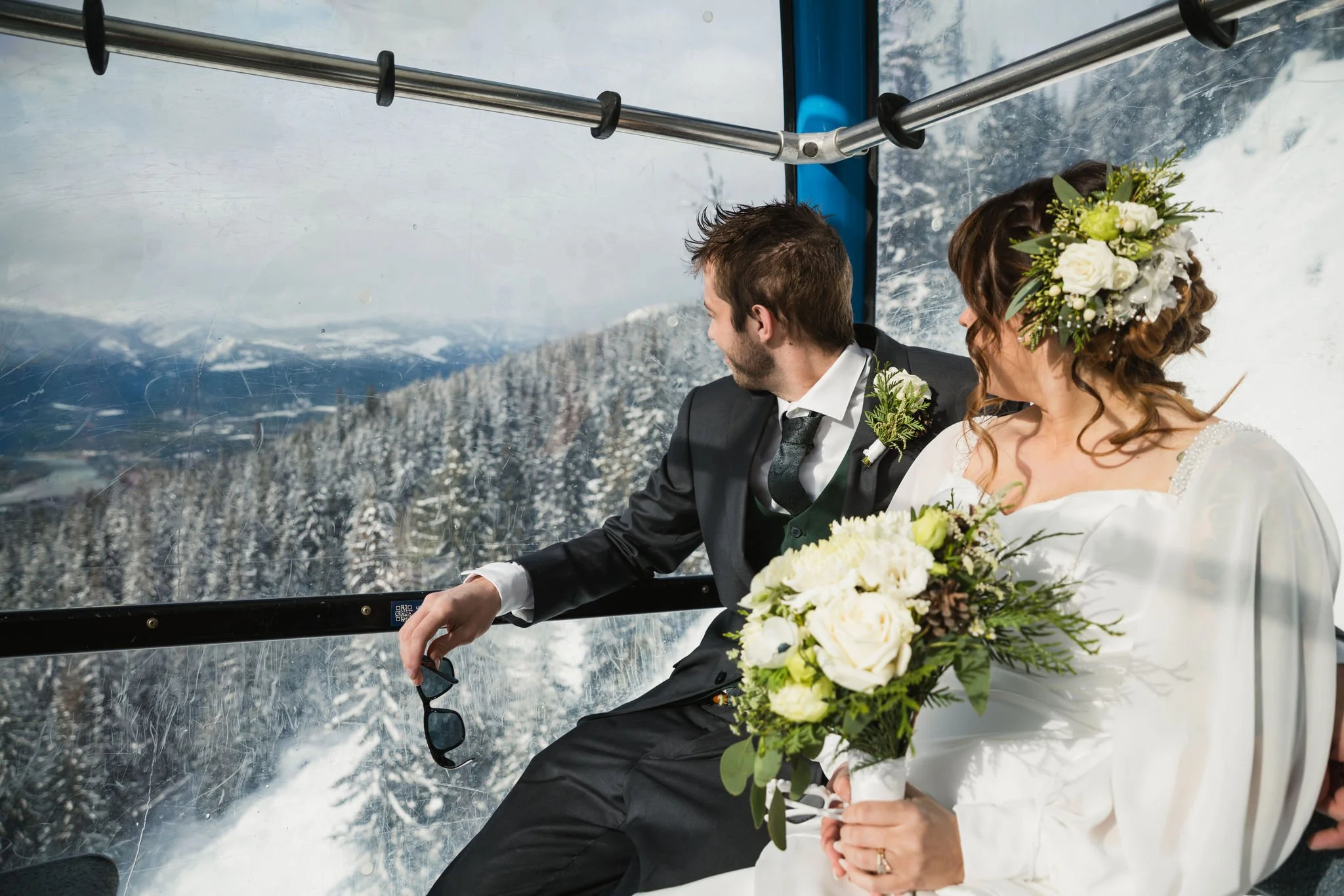 wedding couple in gondola looking out at snow covered mountains