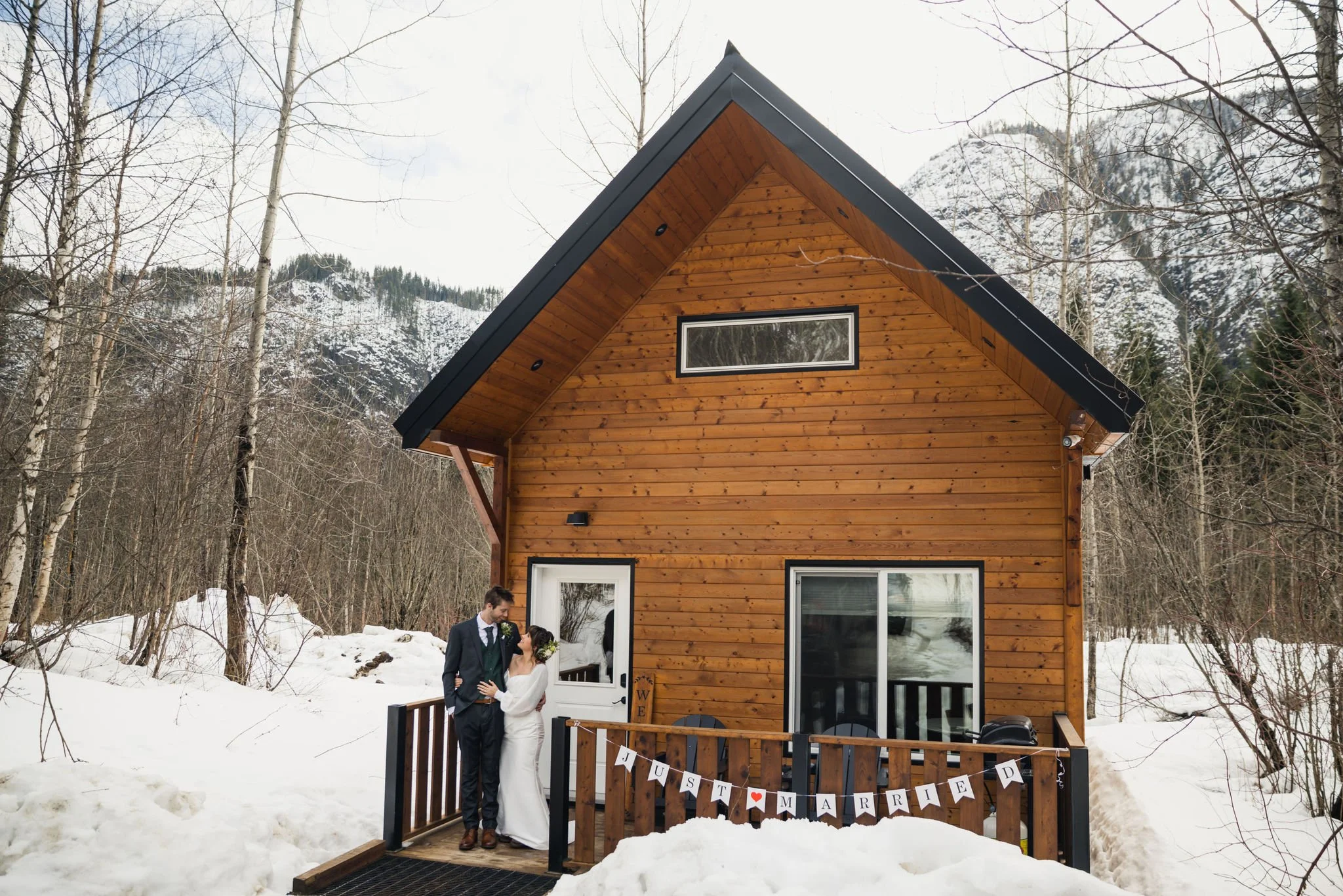 wedding couple standing in front of mountain cabin in winter with just married sign
