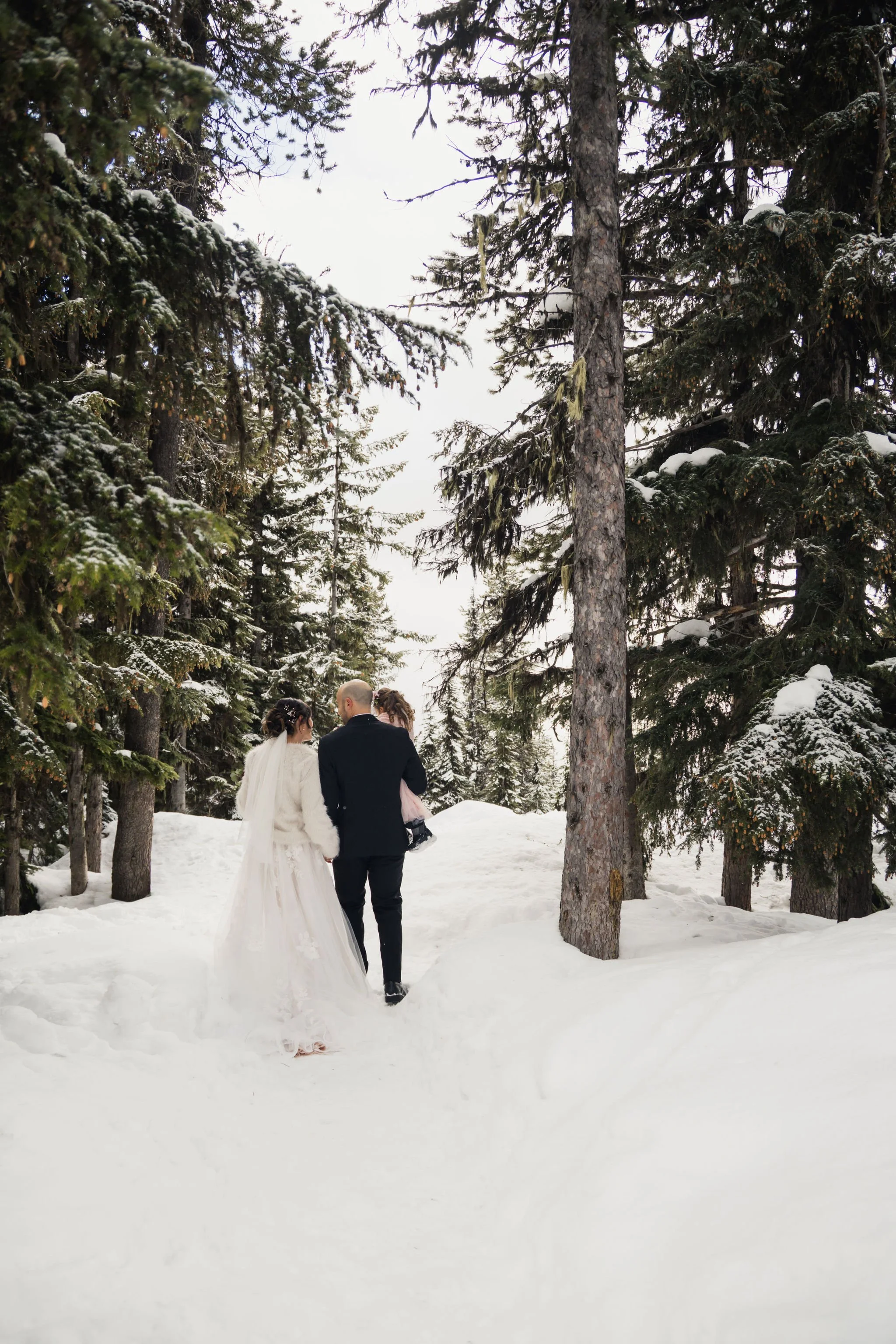 family in wedding attire walks through a forest covered in snow