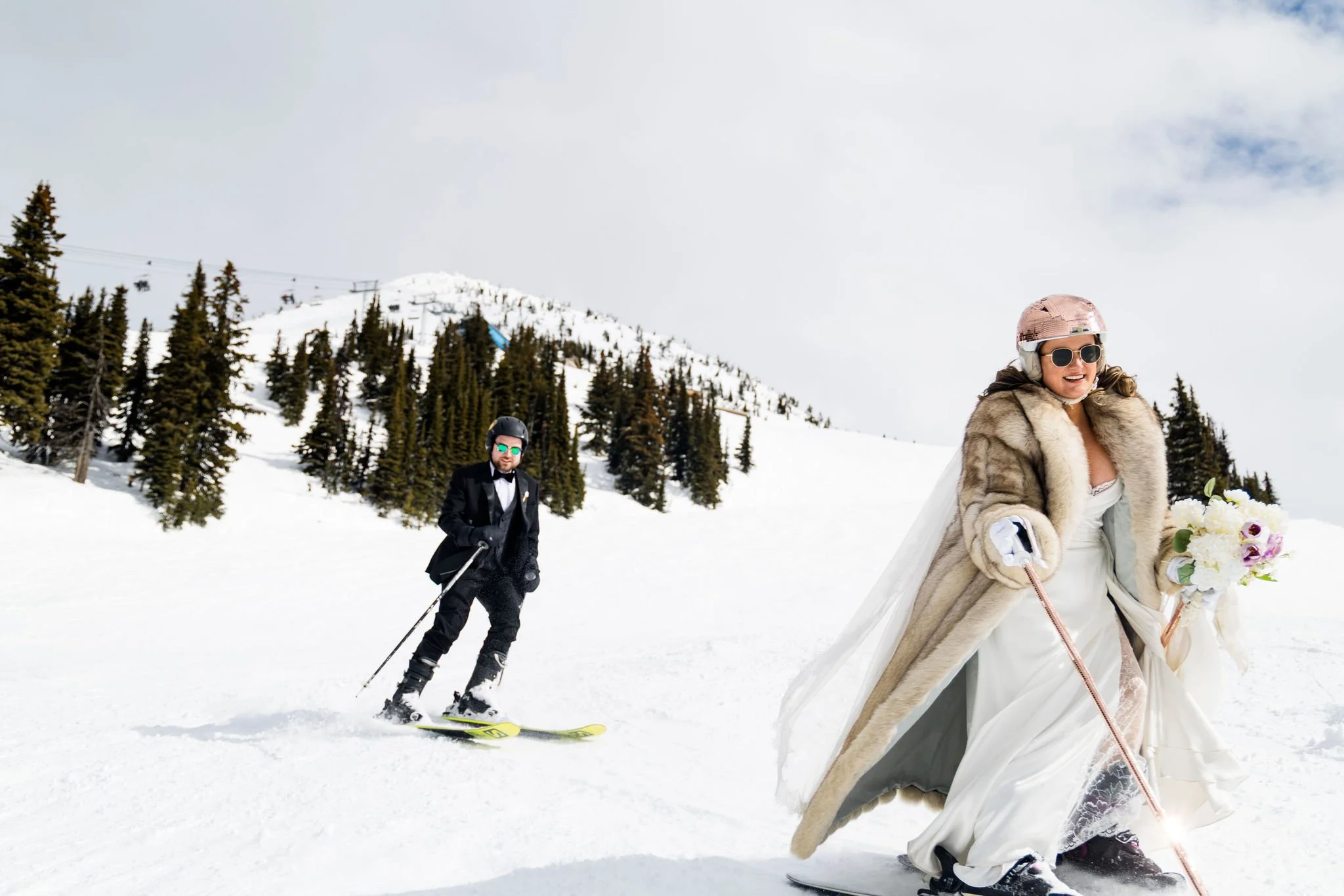 couple in wedding dress and suit ski down a mountain