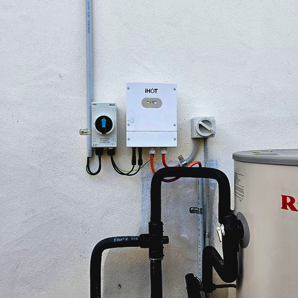 Outdoor wall with electrical and plumbing equipment, including a power meter, a white electrical box, and black pipes.