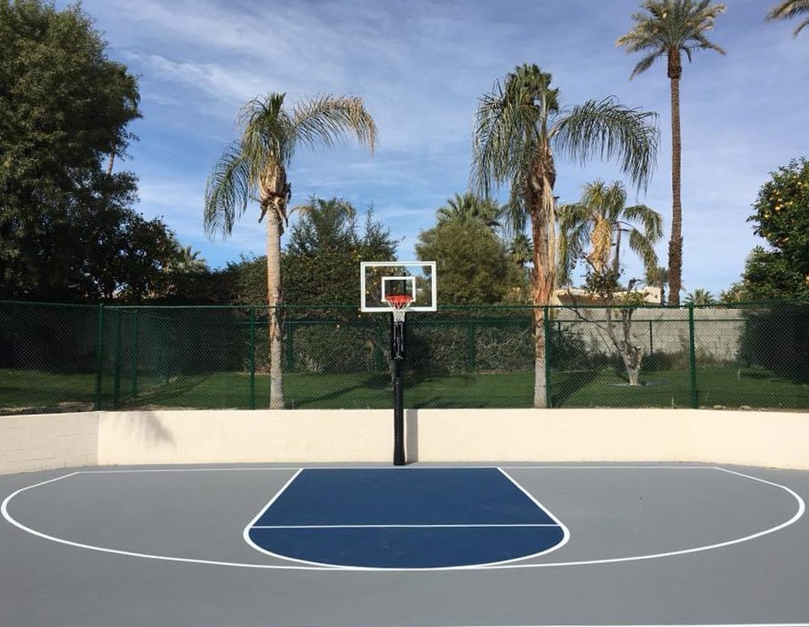  A half basketball court that has a gray surface with a dark blue free throw lane. The court was installed by Palm Springs Tennis Courts. 