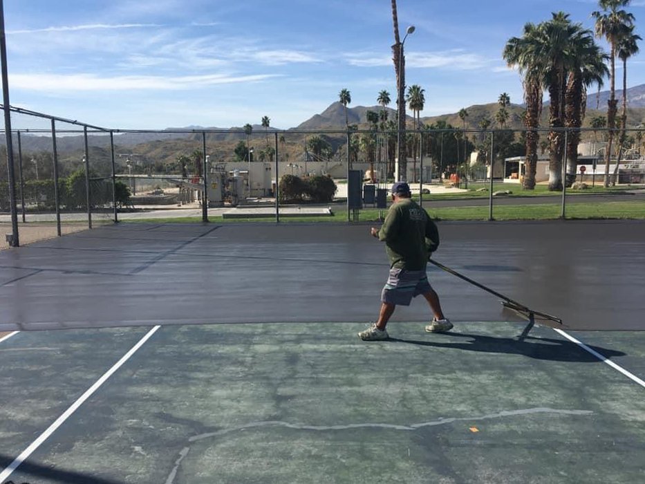  A team member of Palm Springs Tennis Courts uses a squeegee to spread the new surface material over an old tennis court 