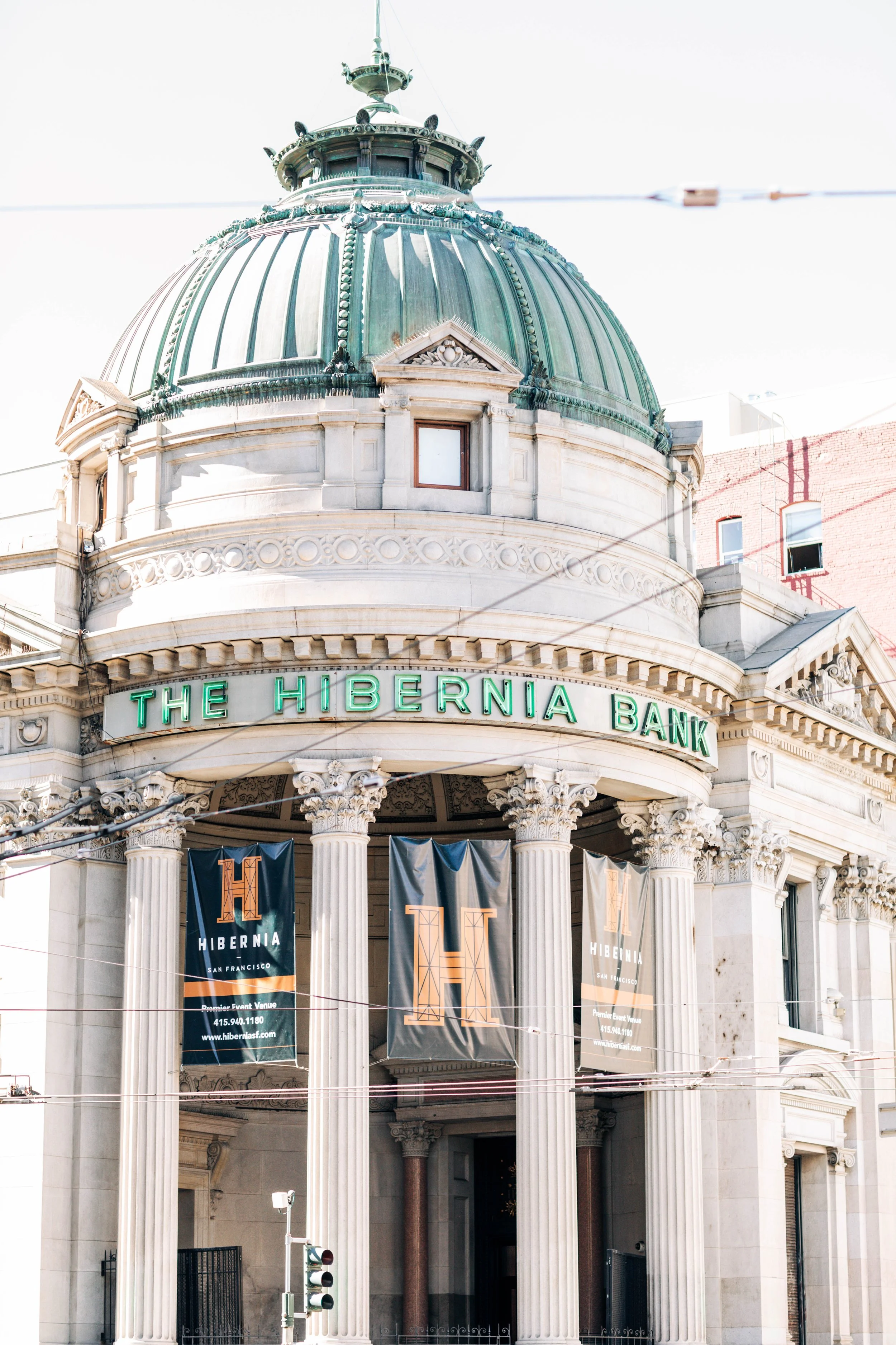 Front view of an ornate historic building with a large green dome, columns, and banners, with illuminated sign reading 'The Hibernia Bank'.
