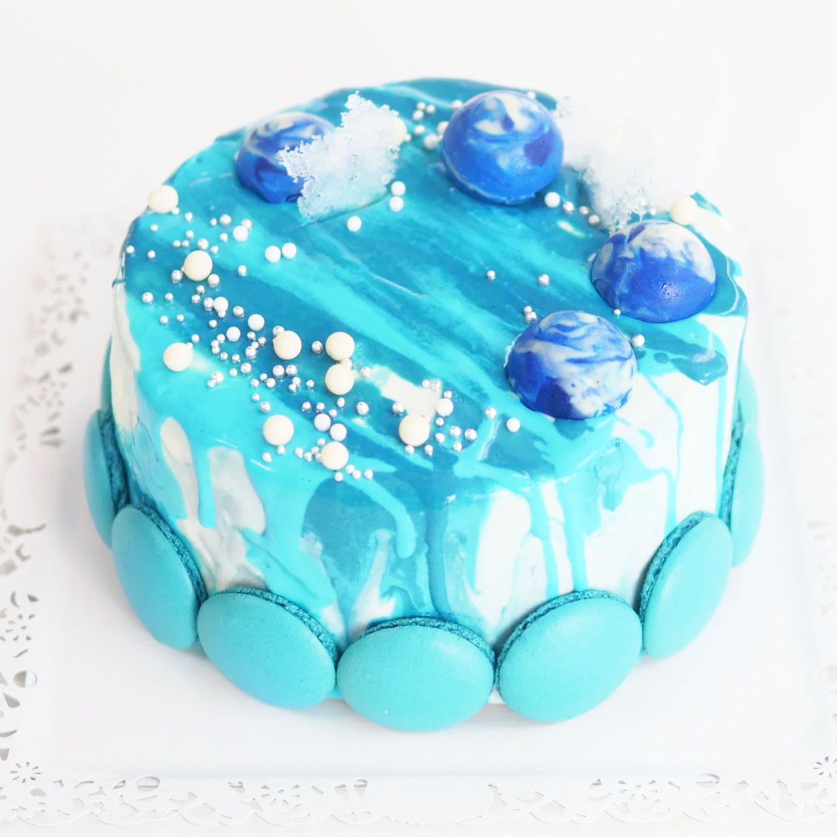 青と白の海の模様がある丸いケーキに、青い球体と白い砂の飾り、白と銀のビーズがトッピングされている。