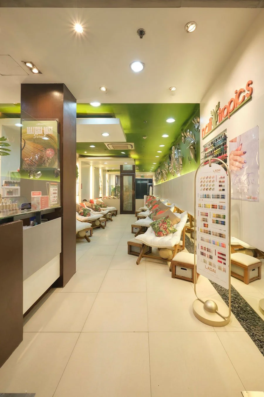 Spa lounge area with white lounge chairs, green leaf pillows, and decorative large leaves in vases on the walls.