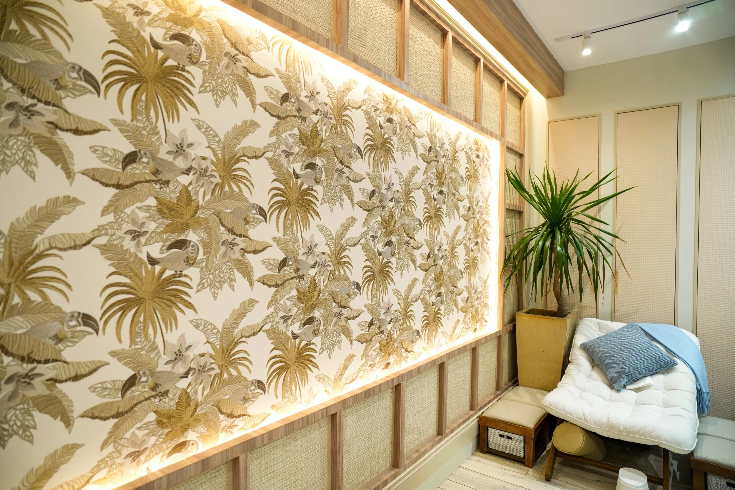 Spa waiting area with reclined chairs, cushions, and blue blankets, featuring decorative wall design and potted plant.