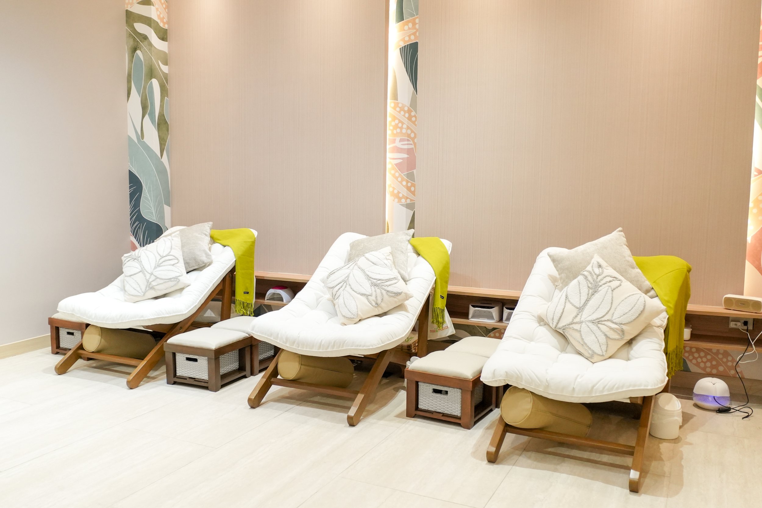 Spa waiting area with reclined chairs, cushions, and blue blankets, featuring decorative wall design and potted plant.