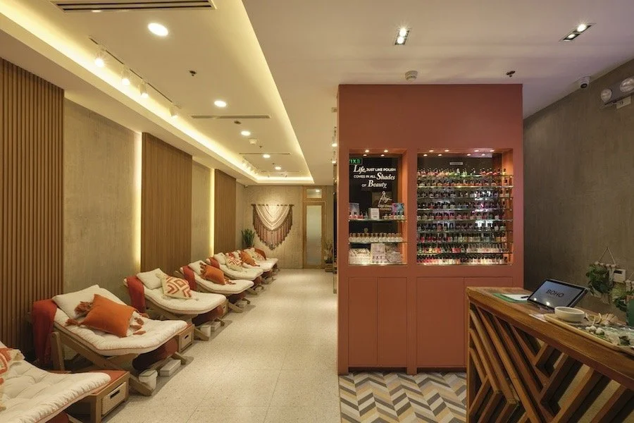 Interior of a modern nail salon with comfortable reclining chairs, cushions, a display of nail polishes, and wall decor.