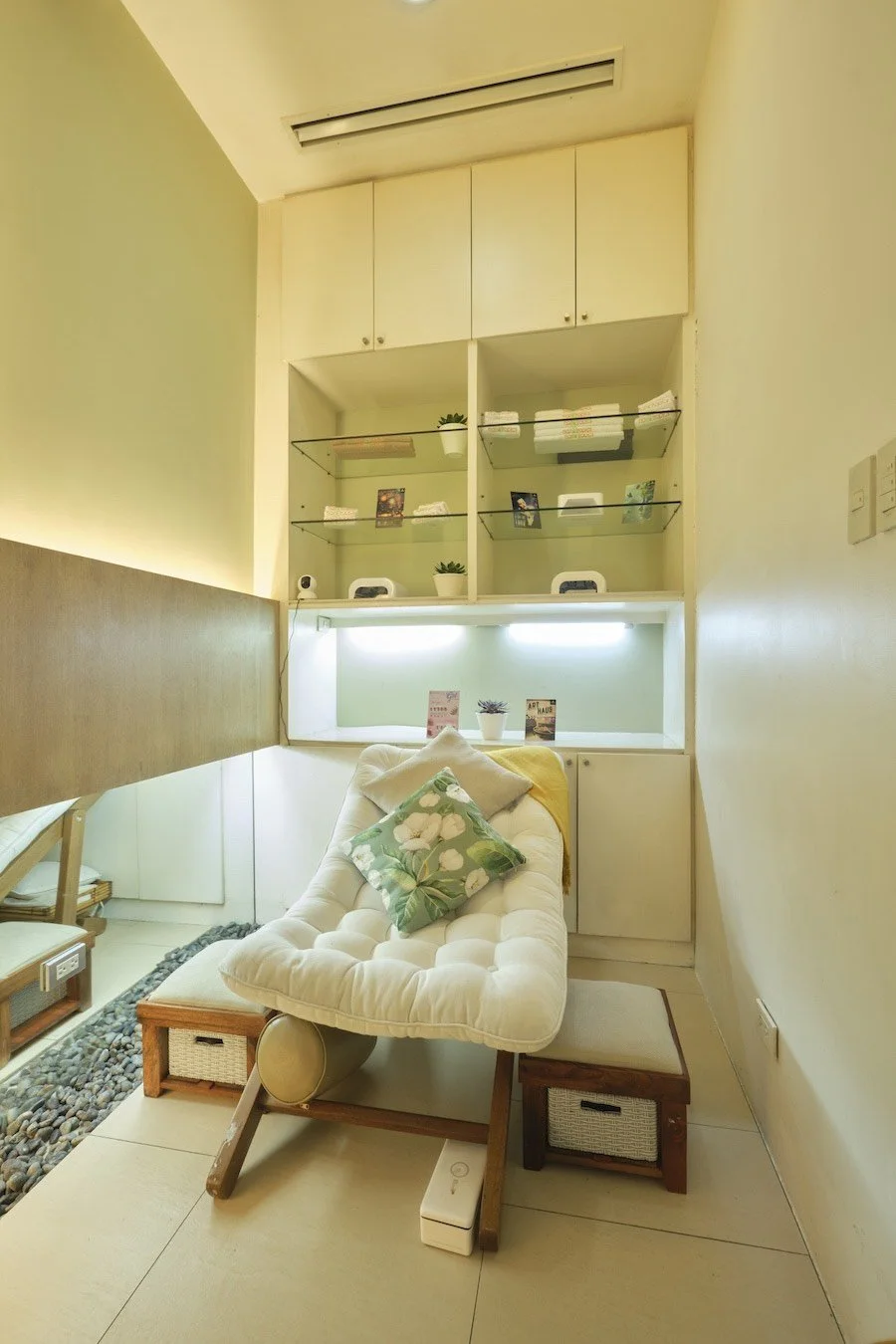 Spa treatment room with a reclining chair, floral cushion, and shelves with spa products and towels.