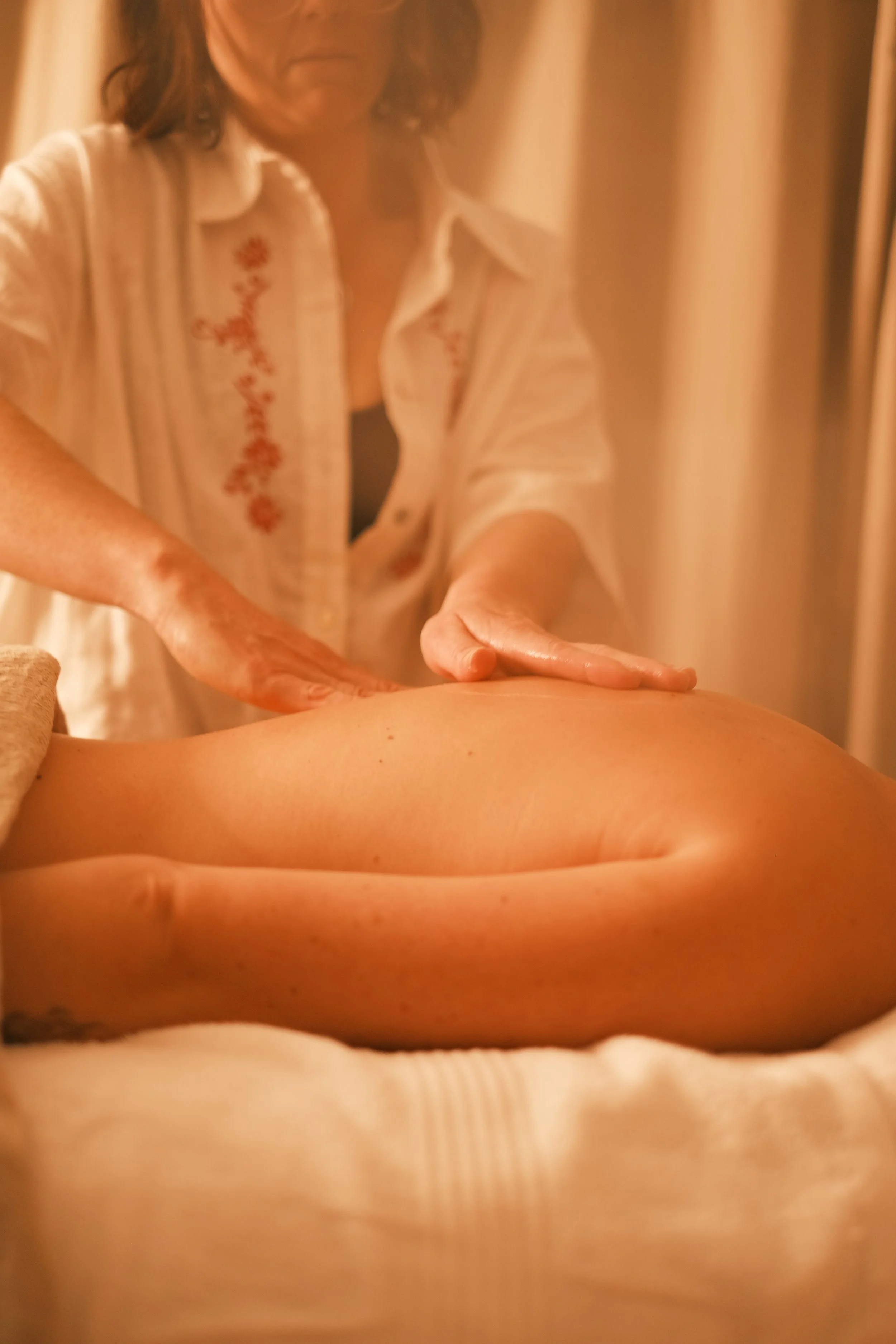 A person receiving a massage, with their back exposed and a massage therapist applying pressure to their back.