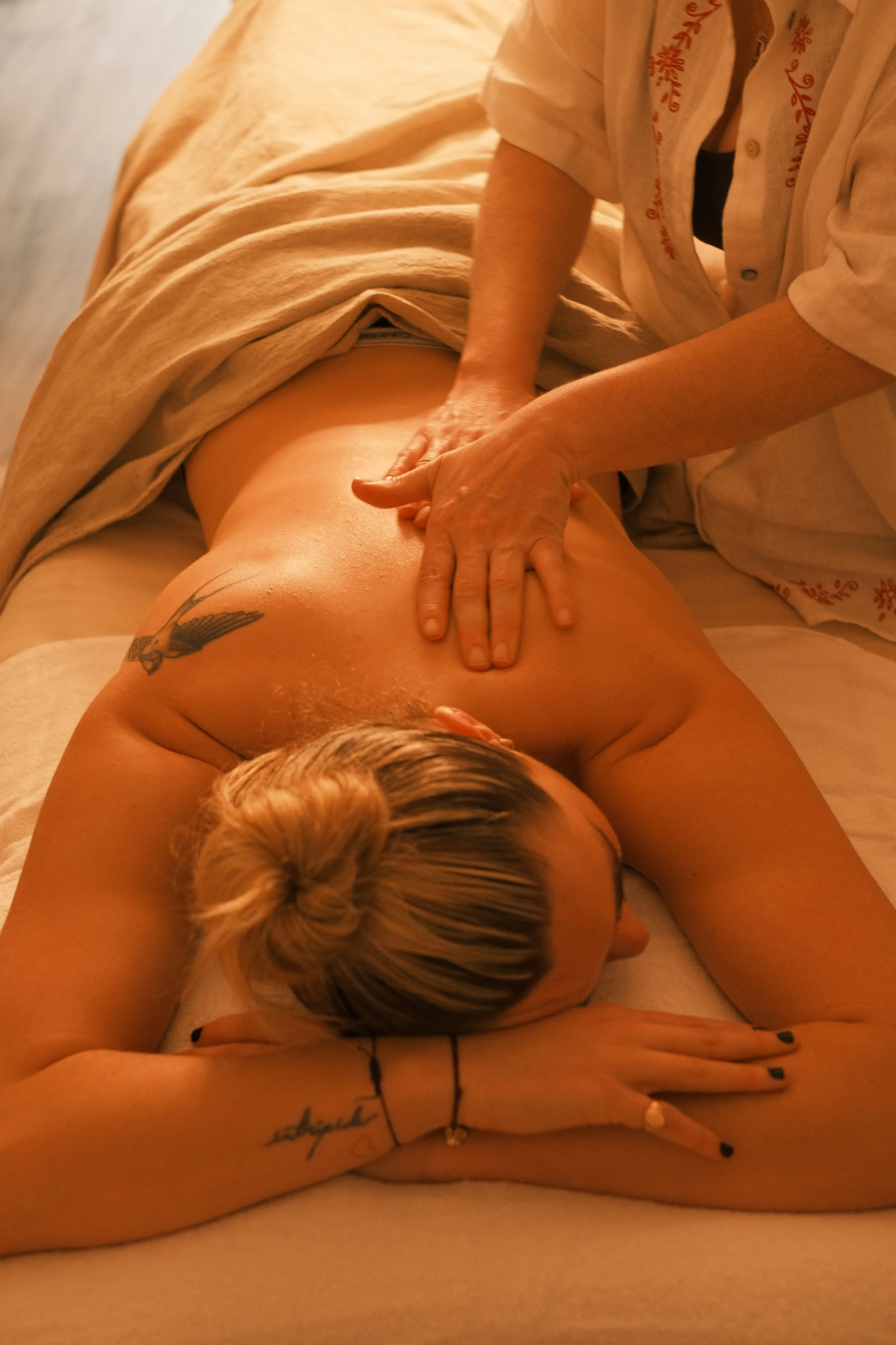Person receiving a massage on their back while lying face down on a massage table, with a blanket covering their lower body.
