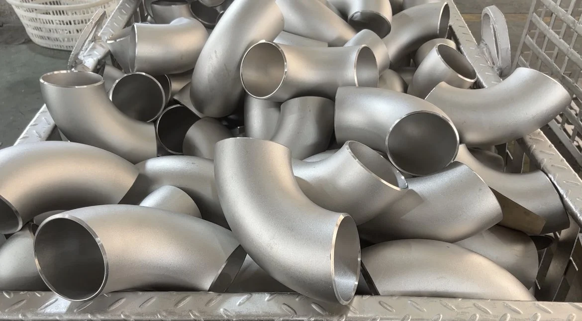 A large metal bin filled with various stainless steel pipe fittings, including elbows and connectors.