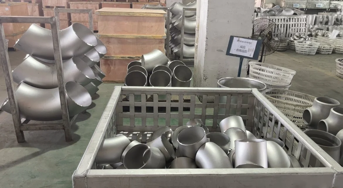 ASTM Stainless steel pipe fittings, including elbows and connectors, stored in a factory or warehouse.