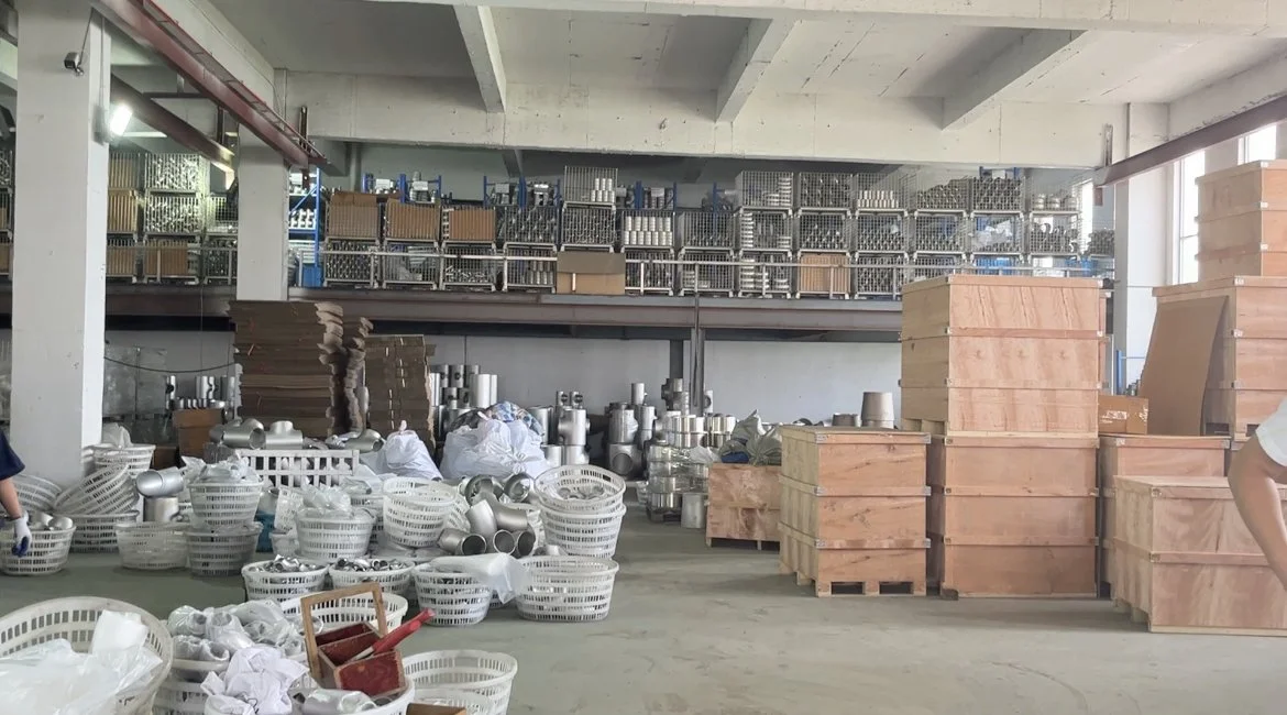 Warehouse with metal and wooden parts, plastic baskets, and equipment stored on pallets and shelves.