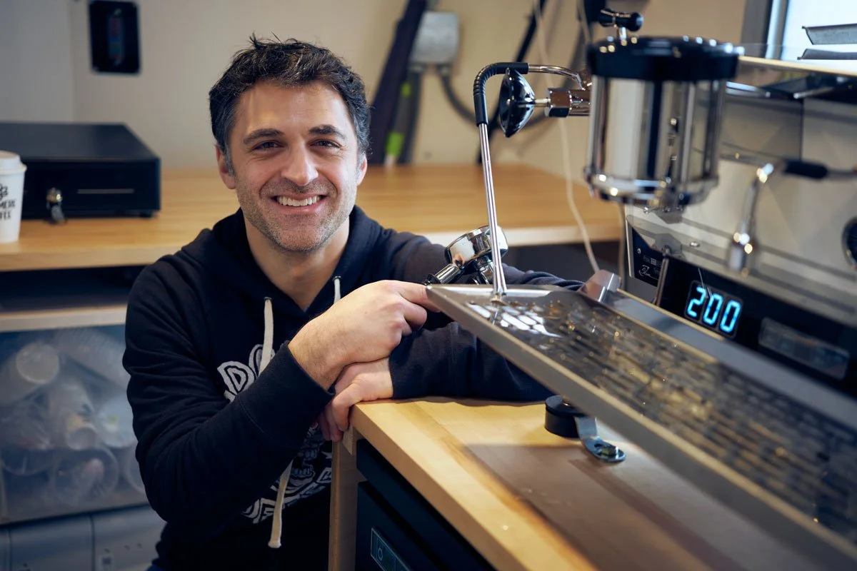 Zack from Edgemere Coffee next to coffee machine in restaurant location