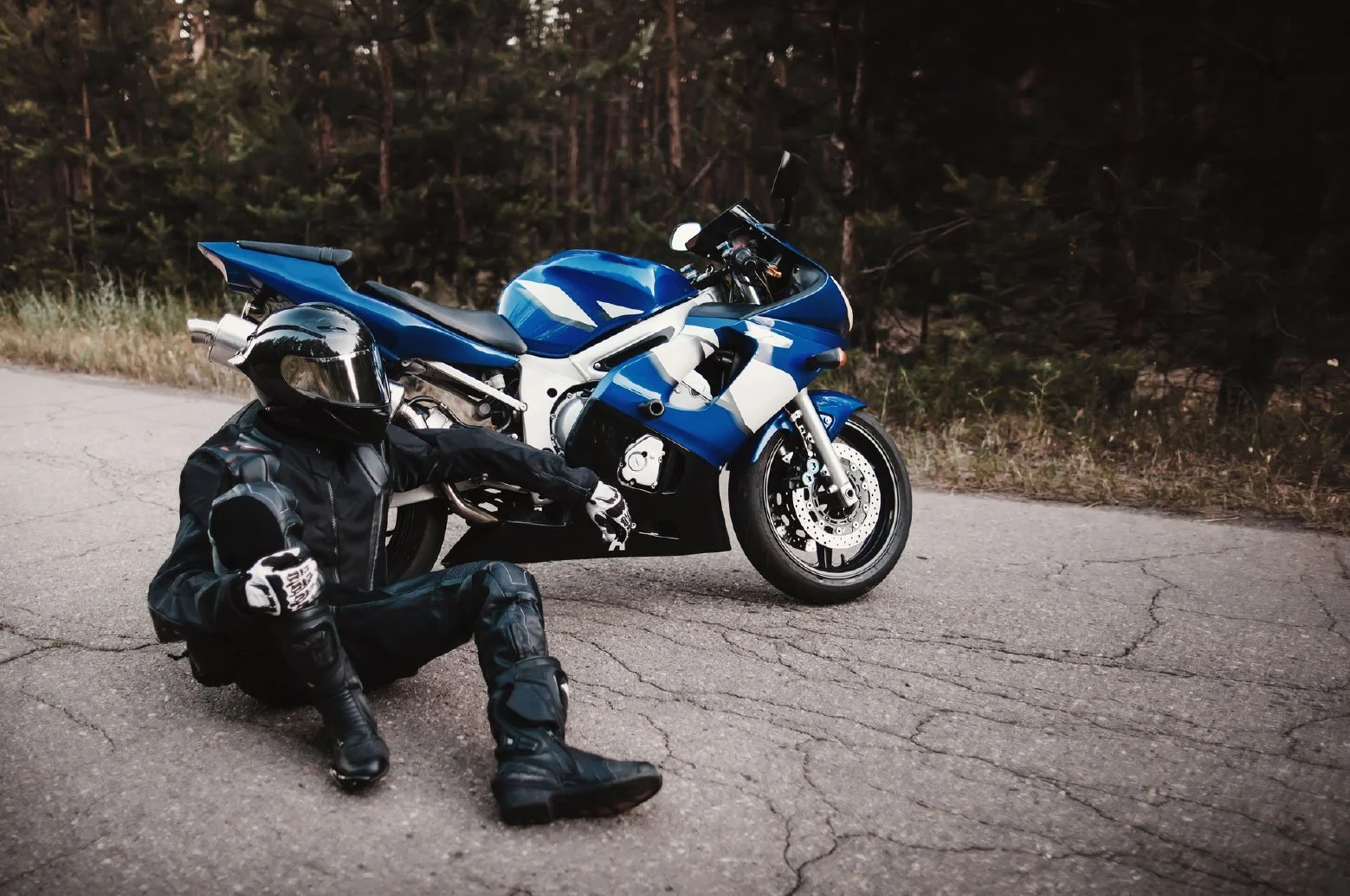 Motorcyclist sitting on pavement next to blue motorcycle