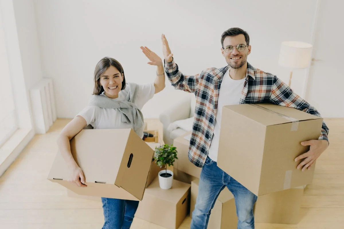 two people holding packing boxes doing a high-five moving into their home
